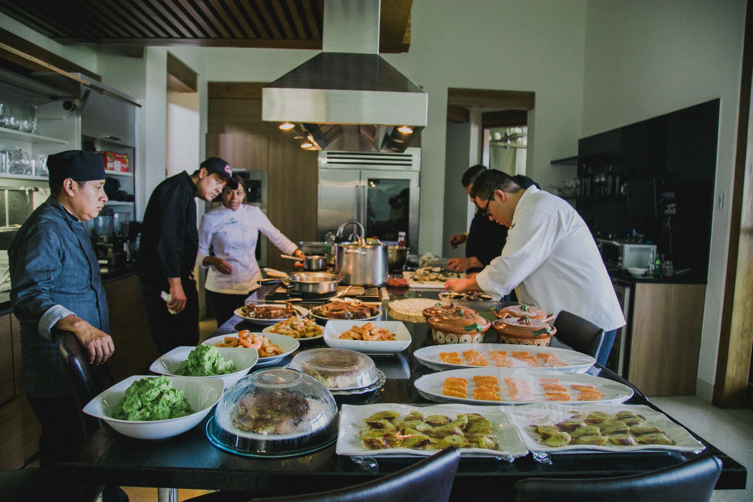 A team of chefs preparing a diverse array of dishes on a kitchen counter indoors.